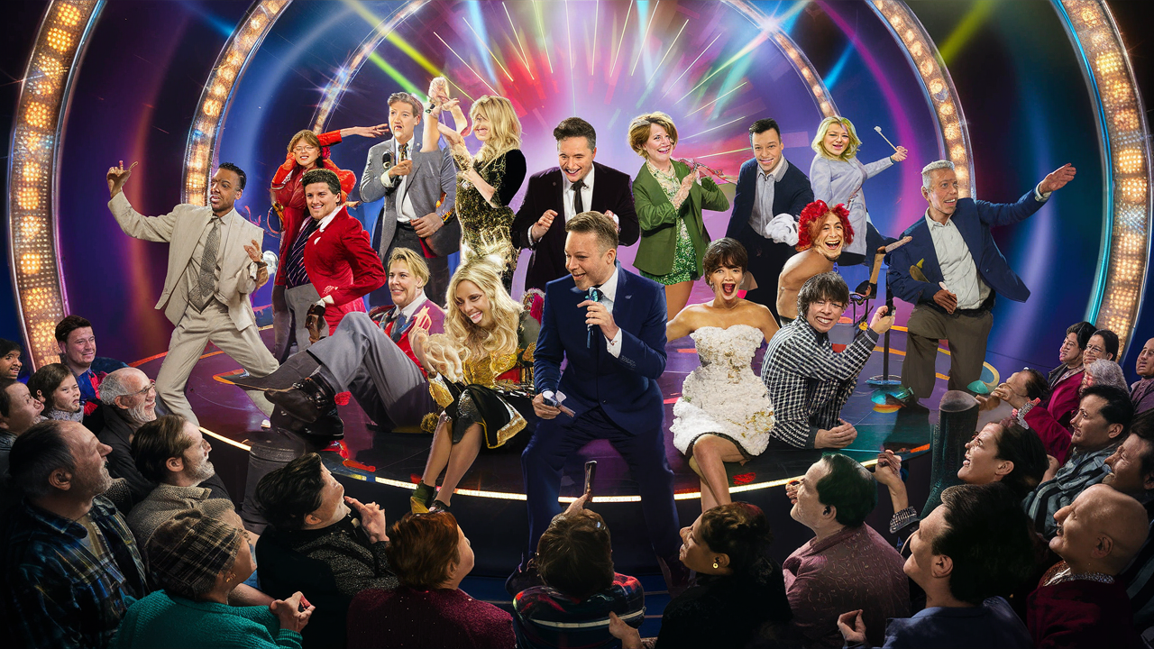 This image depicts a vibrant and energetic scene, reminiscent of a theatrical or television variety show. In the center, a man in a blue suit holds a microphone, suggesting he is the show's host. Surrounding him are various performers in dynamic poses and elaborate costumes, some in formal wear, others dressed whimsically, portraying a wide array of characters, such as a bride in a white dress, a man in a red tailcoat, and another in a checkered jacket. Bright, colorful stage lights create a festive atmosphere, and a cheering audience is seated around the performers, some looking amused, others clapping or gesturing towards the spectacle. The background showcases a dazzling, circular stage set with neon lights, conveying a sense of grandiose entertainment and joyous celebration.